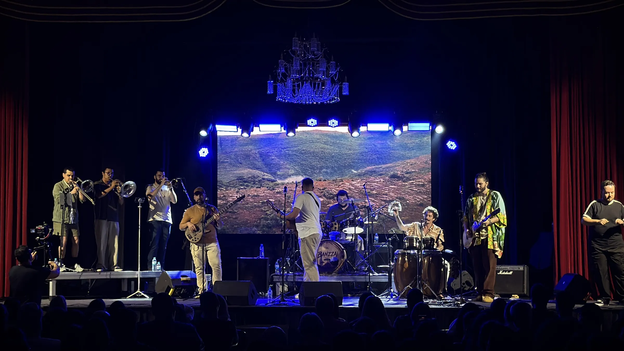 Banda no palco diante do telão com paisagem, sob luz azul